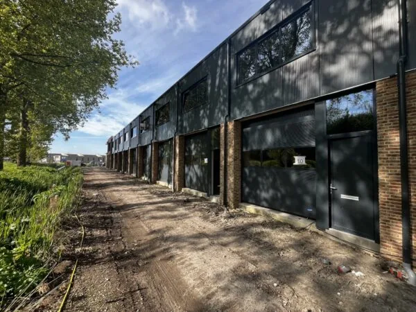 Nieuwbouw bedrijfsunits aan de Broekdijk West 19-10, gelegen langs een onverharde weg met bomen en groenstroken.